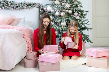 Excited Girls Opening Christmas Gift Boxes. Two girls in red dresses enthusiastically opening pink...