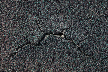 Detailed image of a green and black cracked asphalt road surface.