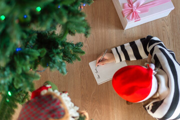 Child Writing Letter to Santa Near Christmas Tree. Overhead view of a child wearing a Santa hat,...