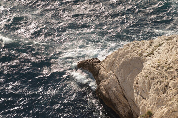 Rocky coastline with crashing waves and sparkling ocean surface in sunlight