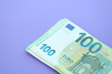 Big amount of one hundred euro money bills on lilac background