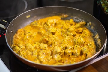 Chicken stewed in sauce with spices in a frying pan on the stove. Delicious chicken dish