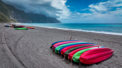 Colorful kayaks lined up on a sandy beach in Taiwan beside vibrant blue ocean waters