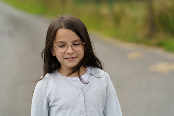 Cute little girl in glasses walking along a country road. Concept of happy childhood in nature.