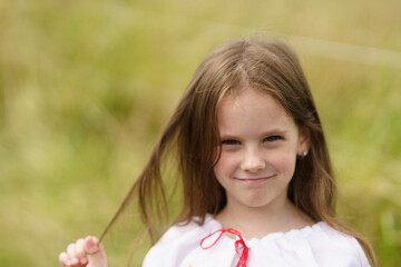 Little cheerful girl in traditional national embroidered shirt stands on blurred green natural...