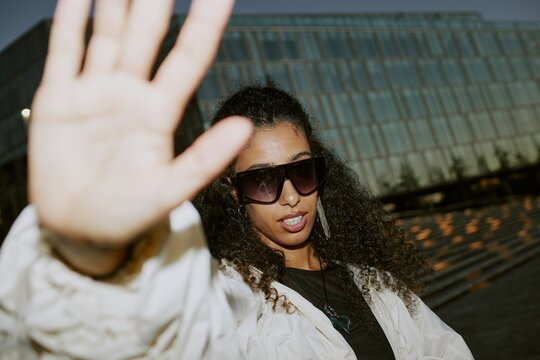 Paparazzi shot of glamorous Middle Eastern female celebrity wearing trendy sunglasses keeping privacy hiding with hand from photographers camera light in street at night, camera flash, copy space