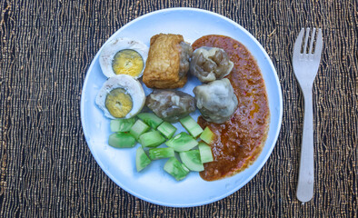 Siomay with egg, potato, and cucumber served on a white plate with a table background. Indonesian cuisine Siomay peanut sauce