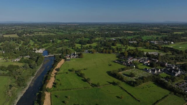 Adare, County Limerick, Ireland, September 2024. Drone orbits counter clockwise in a panoramic overview towards the village with Trinitarian Abbey and cemetery and rural farmland in the distance.