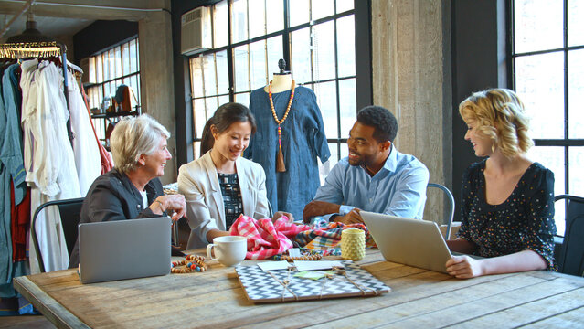 Male And Female Fashion Designers In Studio Meeting Discussing Fabric Swatches
