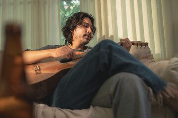 Man Playing Guitar in Cozy, Dimly Lit Room, Relaxing on Couch