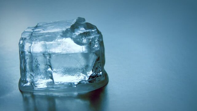 Melting ice cube on blue surface symbolizing global warming and climate change thawing frozen water transparent reflective environment cooling heat natural science