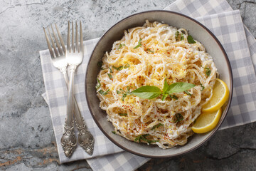 Spaghetti pasta in lemon cheese sauce with ricotta, parmesan and basil close-up in a bowl on the table. Horizontal top view from above