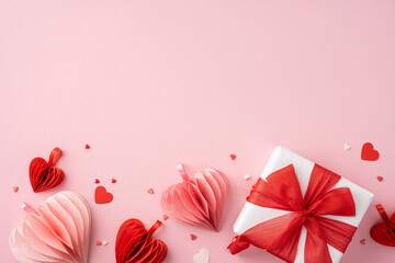 A Valentine's day present wrapped with a red bow, surrounded by red and pink paper hearts on a pink backdrop