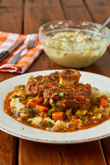 osso bucco served over mashed potatoes topped with a mixed vegetable gravy