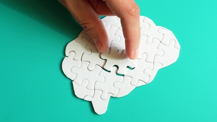 Close-up of a hand placing a missing puzzle piece into a brain shape on a teal background, illustrating cognitive engagement and problem-solving.