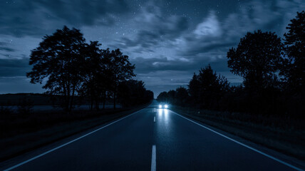 A serene night scene of a lonely road illuminated by oncoming car headlights, surrounded by dark trees under a starry sky.