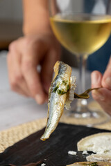 A hand holding a sardine fillet garnished with fresh herbs and a touch of minced garlic, set against a soft focus background, capturing a culinary moment perfectly.