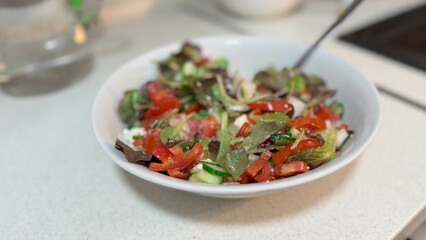 Close-up photo of white ceramic plate with natural fresh vegetable salad. Cucumbers, tomatoes, greens and white Greek feta cheese.