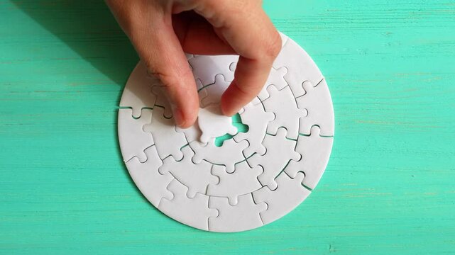 Close-up of a hand taking the final puzzle piece to complete a circular puzzle design on a teal background.