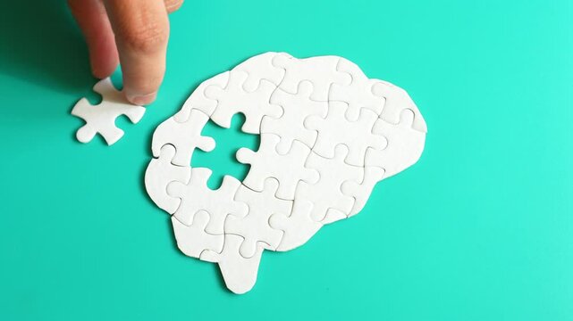 Hand taking and placing puzzle pieces into a brain shape on a teal background, symbolizing mental processes and problem-solving.