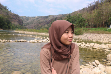 A girl sitting on a river rock smiling. Grounding in the river enjoying the natural scenery