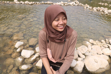 A girl sitting on a river rock smiling. Grounding in the river enjoying the natural scenery