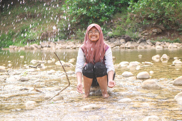 Girl is having fun while splashing water in the river on a sunny summer day. Girl playing water in the river