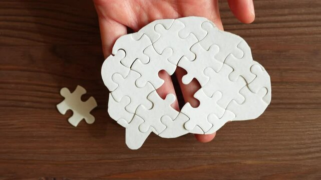 Close-up of hand showing brain-shaped puzzle piece, placing it onto wooden background, and inserting final missing piece to complete the puzzle.