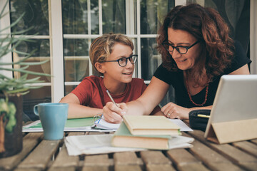 Young student doing homework at home with school books, newspaper and digital pad helped by his...