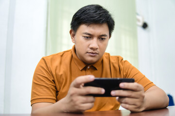 A person wearing an orange shirt is looking intently at a dark-colored smartphone.