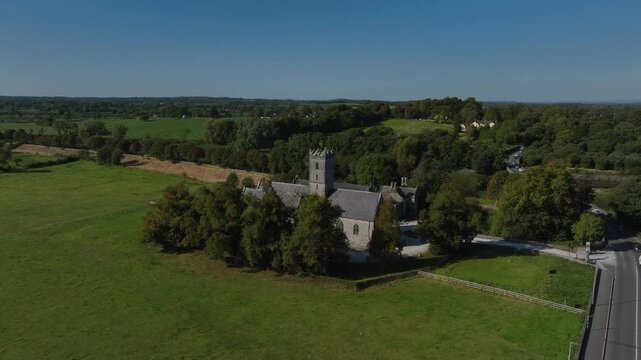 Augustinian Friary, Adare, County Limerick, Ireland, September 2024. Drone orbits clockwise in a medium overview showcasing the architecture between the trees over grassy fields under a clear blue sky