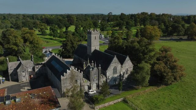Augustinian Friary, Adare, County Limerick, Ireland, September 2024. Drone orbits clockwise in a view from the rear to facade of the gothic building rising to front with grassy field and River Maigue.
