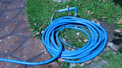 Blue hose on the ground. Flexible plastic hose roll connected to a tap in a sunny outdoor garden with copy space. Selective focus