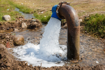 Water flowing from a pipe into a small stream in a rural area under bright sunlight