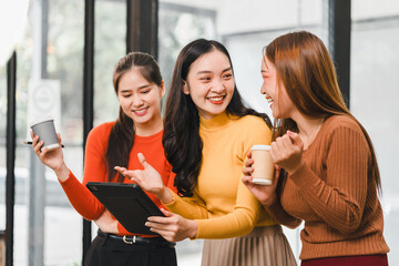 Three women enjoying coffee and tablet in modern cafe, sharing laughter and conversation, dressed in colorful sweaters, creating joyful atmosphere