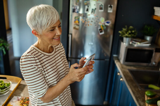 Smiling elderly woman using smartphone in the modern kitchen