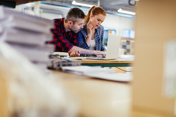 Young man and young woman using a laptop while working in a printing press office