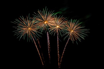 Four green and orange fireworks bursting in unison