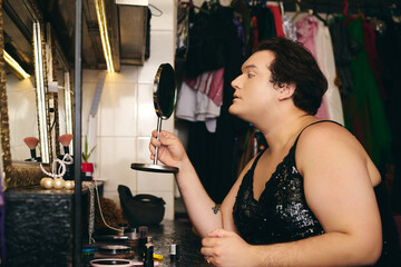 A drag queen applies intricate makeup by a mirror in a vibrant dressing room, ready to shine.