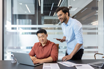 Team working on business project in office. Colleagues using laptop and smartphone for collaborative tasks, reviewing documents, engaging with technology for efficient workflow.