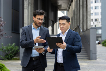 Businessmen discussing work in corporate environment. One holding tablet, another with clipboard,...