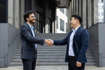 Businessmen shaking hands outside modern building, symbolizing partnership and success. Their smiles reflect mutual trust, cooperation, and positive business relationships, embodying agreement.