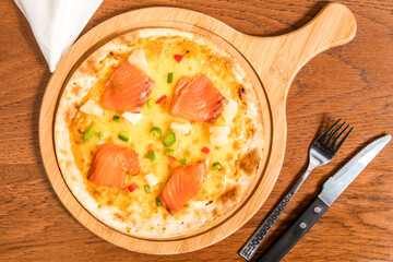 Hawaiian Smoked Salmon Pizza served on wooden board with knife and fork isolated on table top view of italian cousin