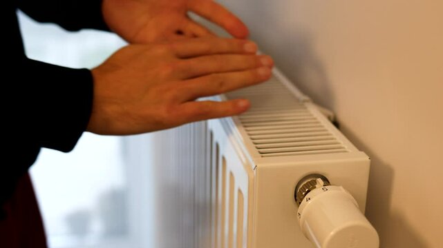 modern radiator for heating in the apartment with power regulators. ideal for those costs of heating and utilities in winter, a man brings his hands in a warm sweater to the radiator to check how hot 