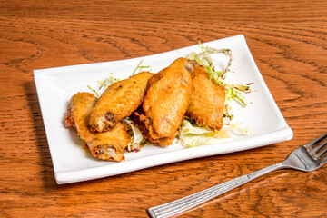 Lemon honey chicken wings with cabbage served in tray dish with fork isolated on wooden table side view of fast food