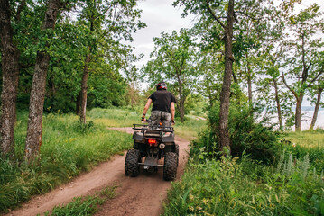 Fototapeta premium a girl and a guy bikers ride quad bikes in a beautiful green forest on a river cliff, their dogs are running nearby