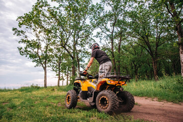 Obraz premium a girl and a guy bikers ride quad bikes in a beautiful green forest on a river cliff, their dogs are running nearby