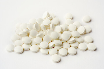 Close up photograph of a pile of white round shaped vitamin, tablets or pills isolated on light background