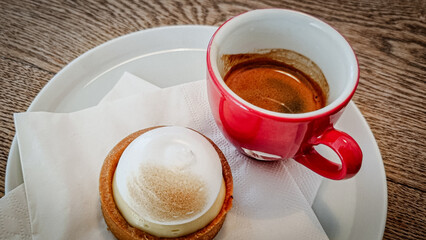 delicious lemon tart served with an espresso in a red cup, white napkin, white dessert plate, wooden table