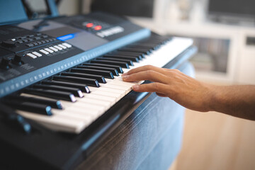 Close-up of hands playing a digital keyboard under warm natural light, capturing the essence of...